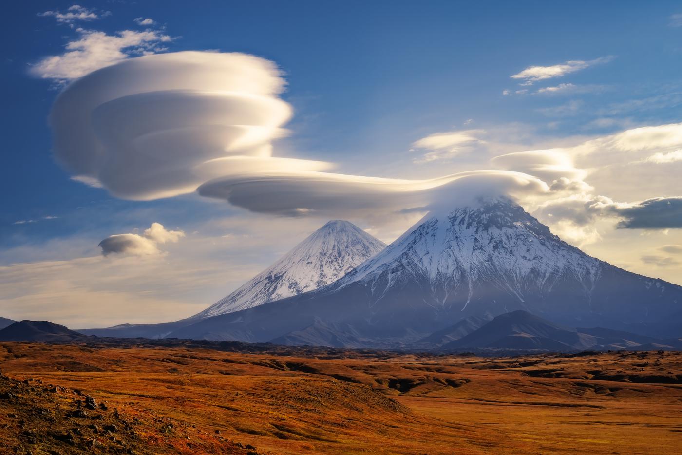 Облака вулканов. Эту фотографию, сделанную на Камчатке, автор описывает так: "В многокилометровой радиалке до каньона реки Студёной открылись Ключевская сопка и вулкан Камень, а сбоку на них решили присесть и укутать лентикулярные облака".