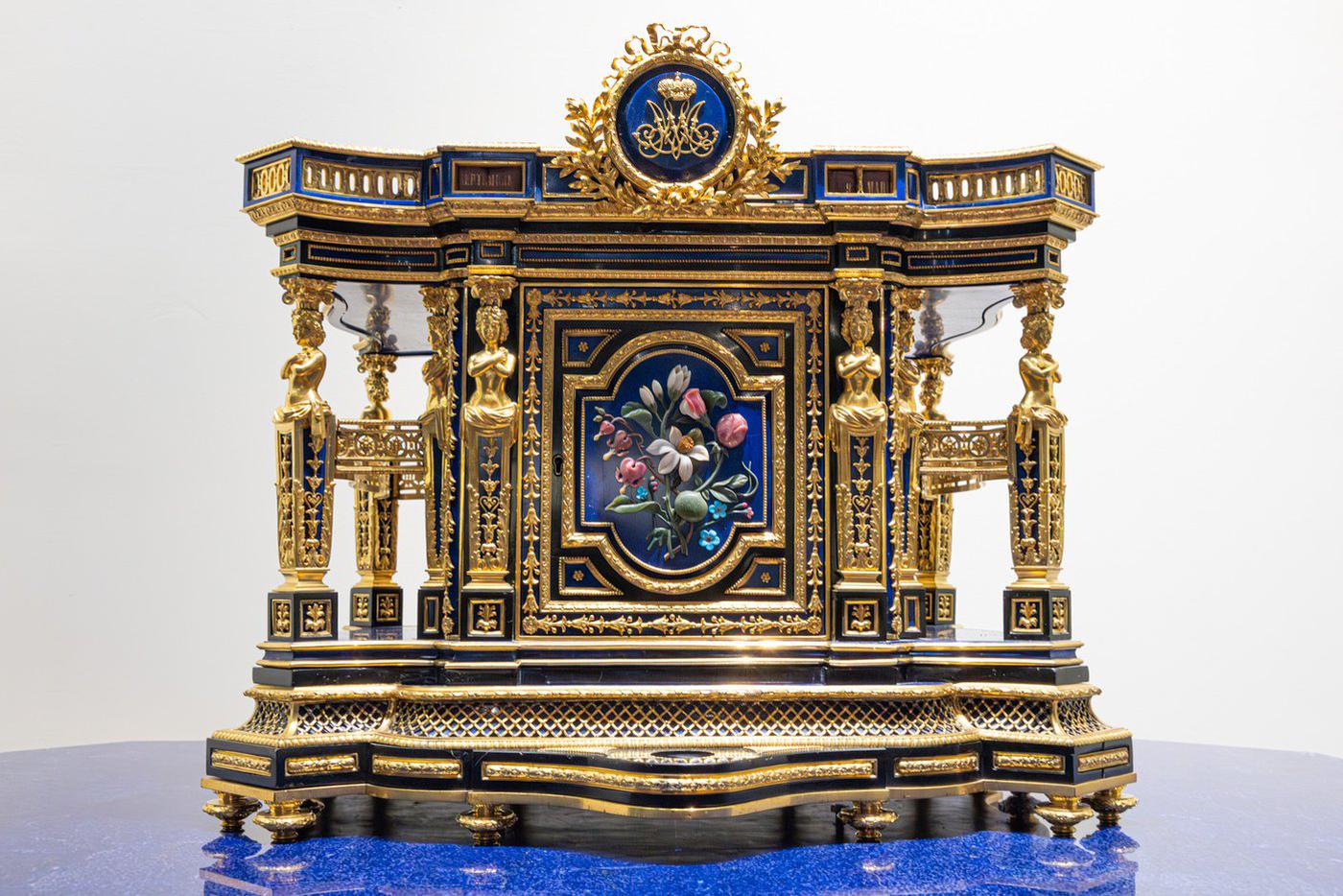 Секретер настольный, 1862 год. Выполнен по заказу императрицы Марии Александровны для Лионской гостиной. Центральная дверца украшена рельефной мозаикой в виде букета цветов, выполненных из полудрагоценных камней: бирюзы (незабудки), кахолонга (цветы магнолии), родонита и яшмы (сердцецвет, душистый горошек, бутон розы), нефрита (стебли и листья).