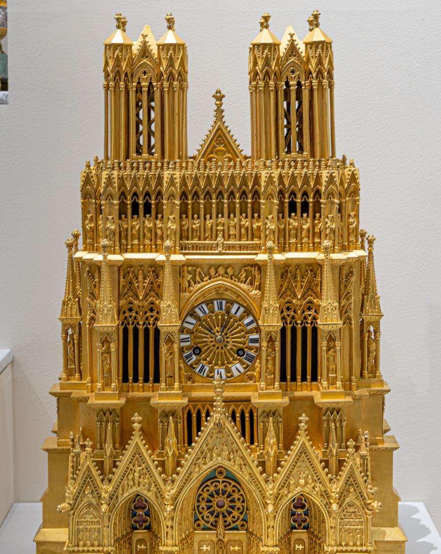 Часы каминные "Реймсский собор". Париж, около 1835 года. Корпус часов воспроизводит западный фасад собора в Реймсе, в котором были коронованы почти все французские монархи. При создании модели воспроизведены в мельчайших подробностях архитектурные детали фасада и скульптурные украшения. Тема соборов в изготовлении часов приобрела особую популярность после выхода "Собора Парижской Богоматери" Виктора Гюго.