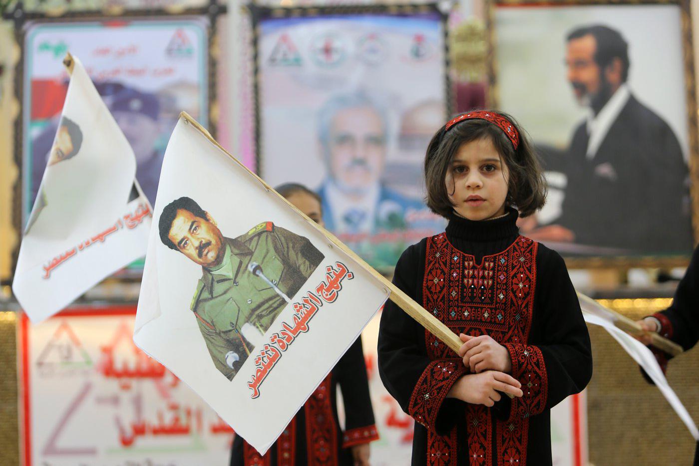 Девочка держит в руках флаг с изображением Саддама Хусейна